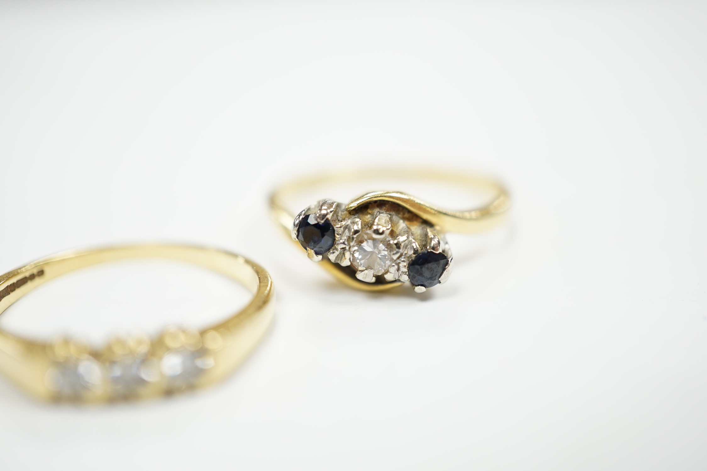 An 18ct gold and three stone diamond ring, size M and an 18ct, sapphire and diamond set three stone crossover ring, size O, gross weight 5.4 grams.